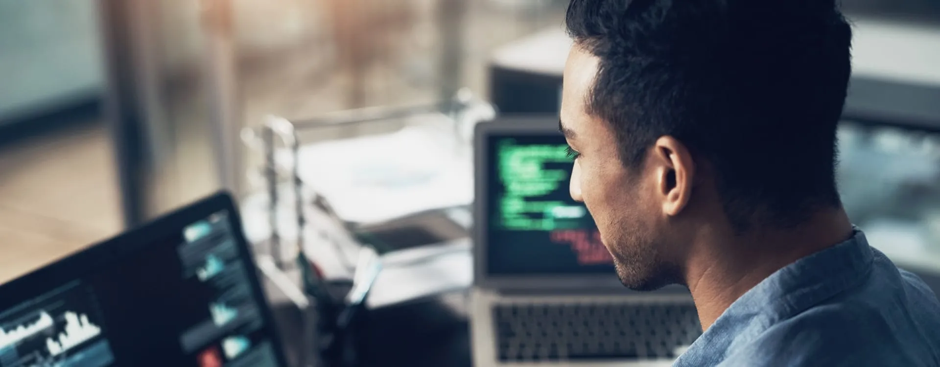 A designer in profile at a desk, looking at a laptop screen showing code.